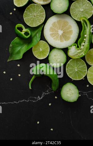 Une image vibrante de limes tranchées, de piments et de grains de poivre disposés sur un fond noir, offrant une touche parfaite de couleur et de texture Banque D'Images