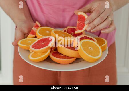 Une femelle dans une chemise rose vif se tient avec une assiette de pamplemousse fraîchement coupée et des tranches d'orange dans ses mains Banque D'Images