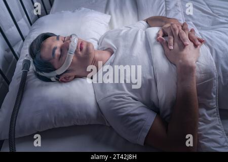 Homme asiatique heureux et en bonne santé portant un masque PPC dormant en douceur dans son lit toute la nuit sans ronfler. Apnées obstructives du sommeil Banque D'Images