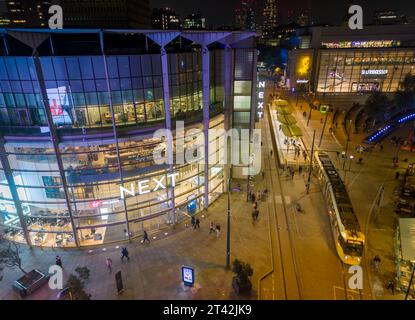 Le tram passe devant le PROCHAIN magasin illuminé la nuit à Exchange Square, centre-ville de Manchester, Angleterre Banque D'Images