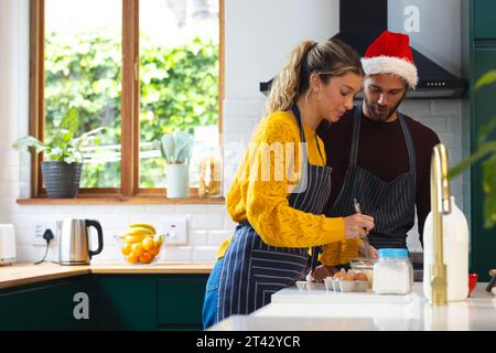 Heureux couple caucasien dans des tabliers et chapeau de noël cuisson dans la cuisine, espace de copie Banque D'Images