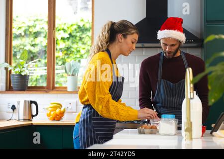 Heureux couple caucasien dans des tabliers et chapeau de noël cuisson dans la cuisine, espace de copie Banque D'Images