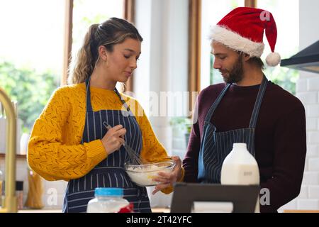 Heureux couple caucasien dans des tabliers et chapeau de noël cuisson et en utilisant la tablette dans la cuisine Banque D'Images