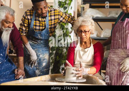 potier féminin biracial concentré avec d'autres, en utilisant la roue de potier dans le studio de poterie Banque D'Images