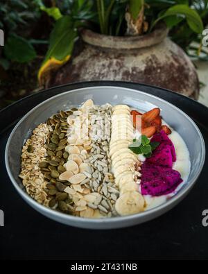 Gros plan d'un bol de yaourt avec des fraises fraîches, des fruits du dragon, des bananes, des noix et des graines Banque D'Images