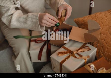 Gros plan d'une femme décorant des cadeaux de Noël enveloppés avec des boules de Noël Banque D'Images