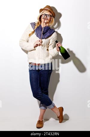 Portrait, femme et tenant la moustache avec du champagne pour la photo ou bande dessinée sur un fond blanc pour le plaisir. Drôle, alcool et fille avec un accessoire à un événement Banque D'Images