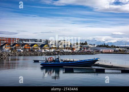 Reykjavik, Islande - 25 septembre 2023 : bateau dériveur bleu amarré dans le port de Karsnes, Kopavogur. Cottages colorés le long de la côte en backgroun Banque D'Images