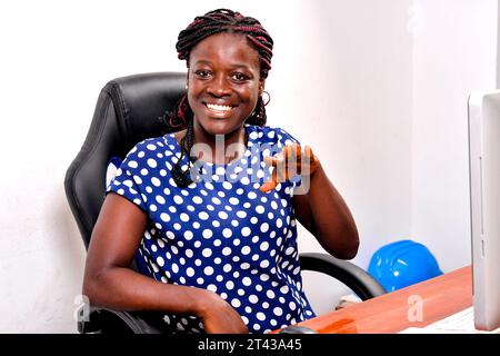 une belle femme d'affaires avec des tresses assis au bureau parlant et faisant le geste de la main rire. Banque D'Images