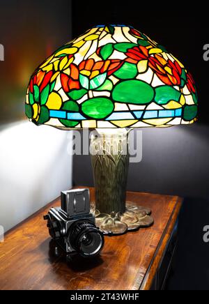 Reproduction lampe Tiffany avec abat-jour acrylique et appareil photo Hasselblad 500 cm moyen format reposant sur un plateau en Cherrywood. Banque D'Images