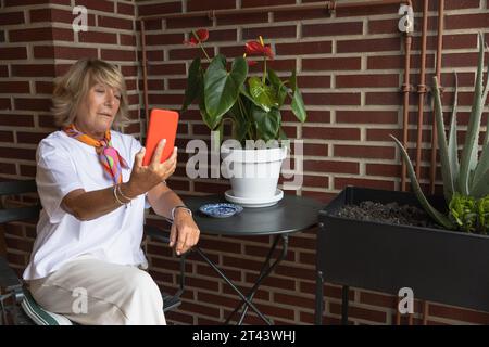 Femme mature assise sur le balcon avec téléphone portable prenant un selfie Banque D'Images