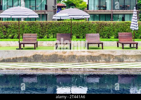 Chaises de détente en bois brun avec de grands parasols à côté de la piscine. Vue sur les chaises de plage placées à côté de la piscine en été. Détente avec Sunbe Banque D'Images