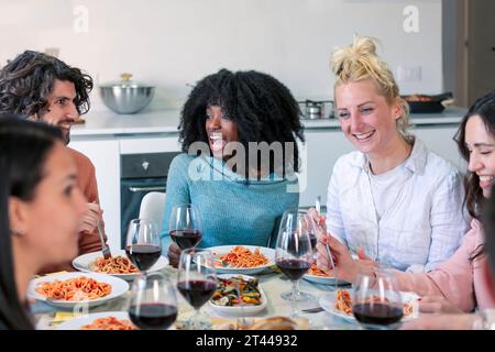 Heureux groupe d'amis mangeant des pâtes au dîner à la maison Banque D'Images