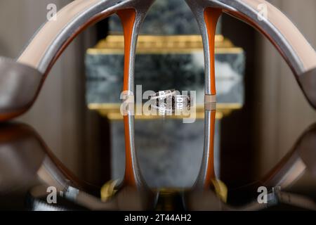 Élégants talons de mariée blancs et bague de mariage sur une surface réfléchissante, avec un décor de pièce luxueusement flouté. Banque D'Images