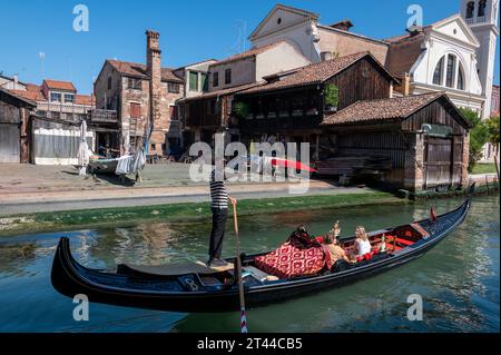 Un gondolier de passage guide sa gondole le long du canal de desserte, Rio de Trovaso, en passant devant une cour de construction de bateaux de gondole du 17e siècle, 'Squero di San Trva Banque D'Images