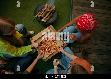 Vue aérienne sur un groupe d'amis mangeant une pizza à proximité brûlant un feu de camp Banque D'Images