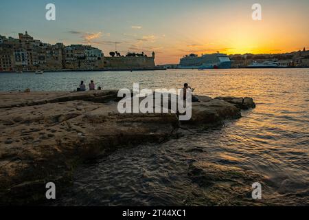 Un homme lit son livre alors que le soleil se couche sur Senglea, l'une des trois villes qui surplombent la capitale de Malte, la Valette Banque D'Images