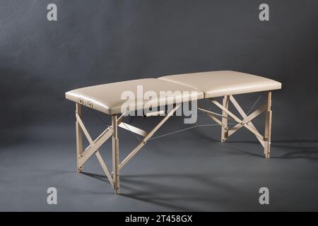 Table de massage pliante portable pour salle de traitement de physiothérapie sur le fond sombre. Banque D'Images
