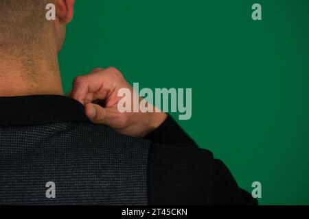 Gros plan des mains d'un homme redressant une chemise noire, il donne gilet d'un costume classique, épaules de différents côtés, mettre trois photos sur un fond vert chromakey gros plan cheveux noirs jeune homme Banque D'Images