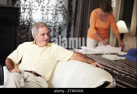 Hôtel, homme senior et femme emballant des vêtements dans la chambre à coucher sur le chat de vacances de retraite ensemble. Voyage, vacances et heureux vieux couple déballer avec lit Banque D'Images