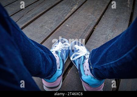 Vous pouvez voir des jambes portant un Jean et des chaussures de sport du point de vue de la fille assise sur le quai en bois, Indonésie, 18 janvier 2015. Banque D'Images