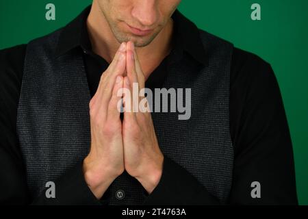 émotions d'un beau gars homme sur un fond vert chromakey gros plan cheveux noirs jeune homme. L'homme inclina la tête en priant Dieu sur un fond noir à la maison. Tenant les mains dans la prière, les yeux fermés. Banque D'Images