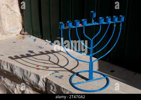 Une Hanukkah menora bleue en métal projette une ombre sur un mur de pierre à l'extérieur d'une maison de Jérusalem dans la journée pendant la fête des lumières en Israël. Banque D'Images
