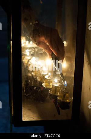 Gros plan de la main d'un homme tenant une bougie et allumant les lampes à huile de la menorah de Hanukkah pendant le Festival des Lumières de huit jours en Israël. Banque D'Images