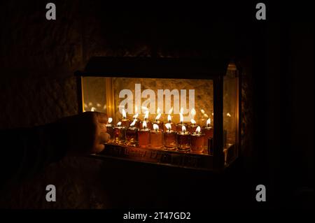 Un homme allume les mèches sur de minuscules fioles d'huile dans une menorah de Hanukkah portant les mots hébreux : « ces bougies, elles sont sacrées », pendant la célébration Banque D'Images