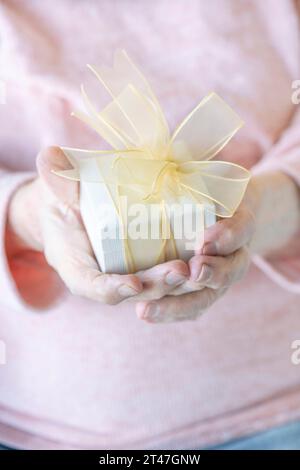 cadeau, gros plan main ridée d'une vieille femme âgée tenant un cadeau blanc ou une boîte cadeau avec ruban. mains de vieillards froissées tenant ou donnant un cadeau Banque D'Images