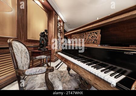 Beau piano à queue en bois verni dans un salon à la décoration saturée, beaucoup de bois sur les murs Banque D'Images