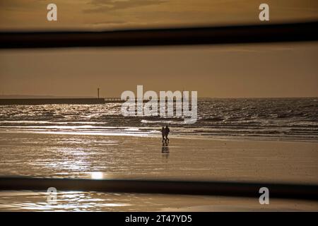 Swansea, Royaume-Uni. 29 octobre 2023. Un couple de promenade le long du bord de l'eau en face de la jetée de Swansea Docks ce matin peu après un lever de soleil orageux le jour où les horloges sont remontées d'une heure, ce qui marque la fin de l'heure d'été britannique. Crédit : Phil Rees/Alamy Live News Banque D'Images