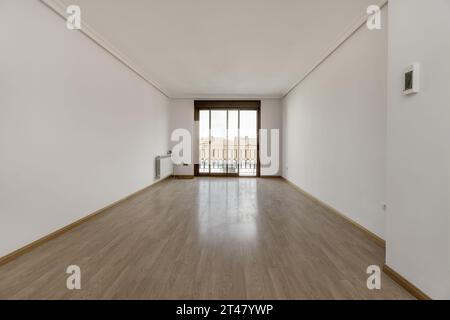 Chambre vide dans une maison avec des murs peints en blanc, des planchers en bois, des radiateurs en aluminium blanc et un grand balcon avec des portes coulissantes en métal et en verre Banque D'Images