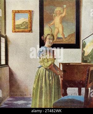 La légende de 1916 se lit comme suit : «Vermeer de Delft 1632-1675 Dutch School Lady at a Spinet dans la Galerie nationale signé J V Meer (et J et M entrelacés) sur le côté de l’épinette peinte à l’huile sur toile 1 pi 8 po. x 1 pi 6 po. » Johannes Vermeer était un peintre hollandais de l’époque baroque qui s’est spécialisé dans les scènes intérieures de la vie de la classe moyenne. Il est considéré comme l'un des plus grands peintres de l'âge d'or néerlandais avec Rembrandt. Banque D'Images