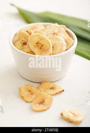 Croustilles de banane séchées jaune collation dans la plaque de bol en verre sur la lumière avec la feuille verte. Banque D'Images