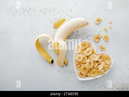 Chips de banane séchées dans une assiette en forme de coeur avec banane crue.vue de dessus. Banque D'Images