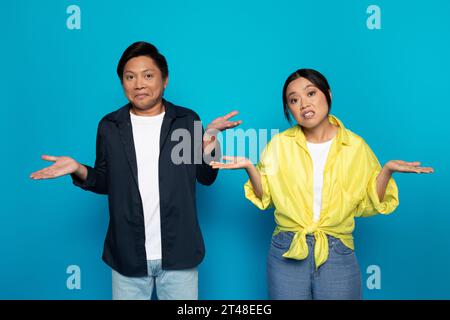 Triste couple asiatique confus millénaire dans Casual étend les mains sur les côtés, tenir l'espace libre Banque D'Images