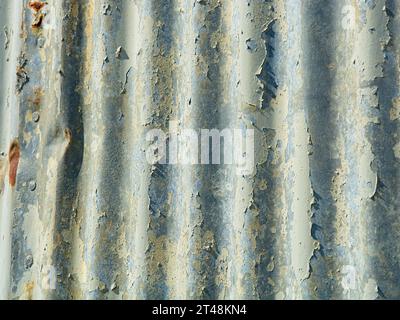 Gros plan sur un revêtement en acier ondulé patiné éclairé latéralement avec des éclats de peinture Banque D'Images