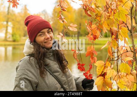 Un beau portrait d'une femme d'âge moyen posant parmi les feuilles de raisin d'automne rouges et jaunes sur le fond d'un étang. Nature automnale. Une promenade dans le Banque D'Images