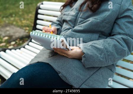 gros plan de mains féminines dessinant dans un carnet de croquis. une fille assise sur un banc et esquissant ses pensées dans un cahier. une atmosphère particulière de creativi Banque D'Images