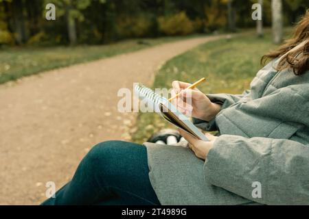 Dessin en plein air. gros plan de mains féminines dessinant dans un carnet de croquis. une fille assise sur un banc et esquissant ses pensées dans un cahier Banque D'Images