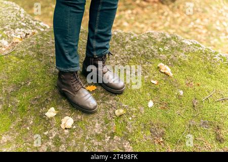 les pieds des femmes en cuir bottes d'automne et jeans se tiennent sur un grand rocher recouvert de mousse verte de la forêt. Marcher dans les bois. Nature et recrea active Banque D'Images