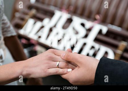 Les mains d'un couple de jeunes MARIÉS avec des anneaux, avec un signe flou "JUST MARRIED". Gros plan, capturant l'émotion et la célébration. Banque D'Images