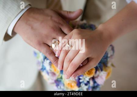 Gros plan capturant un moment d'intimité et de connexion. Il met en valeur les mains des jeunes mariés, en mettant l'accent sur les anneaux de mariage, sur le fond Banque D'Images