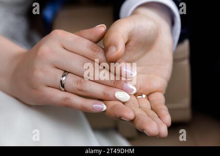 Gros plan de mains entrelacées portant des bandes de mariage, soulignant l'engagement. Doigts délicats de la femme avec vernis rose doux contre la main de l'homme. Symbo Banque D'Images