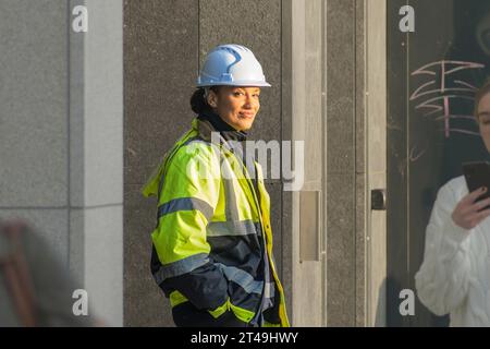 Heureux constructeur. Une jeune femme en veste Hi-Viz et casque protecteur de constructeur dans la rue de Dublin regardant la caméra avec un sourire amical Banque D'Images