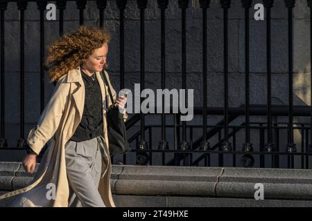 La vie quotidienne. Jeune femme stylée dans la ville avec son téléphone portable tout en marchant dans une rue de la ville. Dublin, Irlande. Banque D'Images