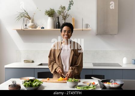 Heureuse fille de chef africain cuisinant des repas végétariens dans la cuisine à la maison Banque D'Images