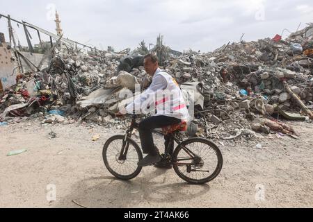 Le Dr Hassan Zein Al-DIN monte son vélo au milieu des décombres alors qu’il se rend à l’école des Nations Unies pour soigner les personnes déplacées par la guerre dans le camp d’Al-Bureij, dans le centre de la bande de Gaza, le 29 octobre 2023. Palestinien Dr Hassan Zein al-DIN, 54 ans, spécialiste de la médecine générale et des maladies chroniques. Il a été déplacé de la ville de Gaza vers la région de Bureij en raison de la guerre. Il se déplace à vélo entre les centres d’accueil pour soigner les déplacés et assurer le suivi de leurs cas au quotidien. Il se rend dans la ville de Gaza pour suivre les cas d'un certain nombre de patients dans les centres d'hébergement laissés par t Banque D'Images