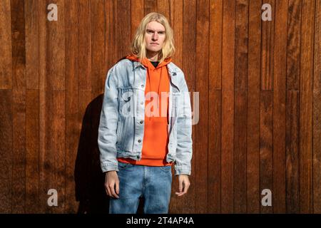 Apathique blond homme à cheveux longs scandinave apparence androgyne se tient près de la clôture en bois. Banque D'Images